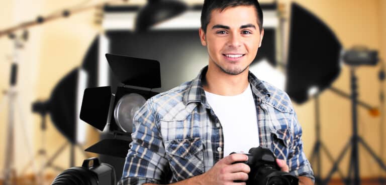 Young photographer with camera on photo studio background