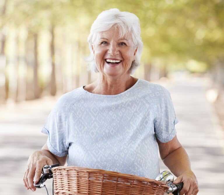 Portrait Of Smiling Senior Woman Cycling On Country Road